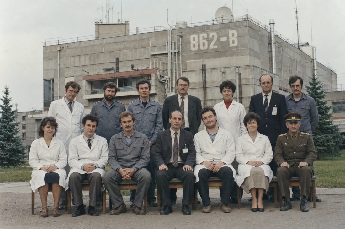 Fourteen Facility 862-B staff arranged in two rows outside the main block, in lab coats, work jackets and suits, with a uniformed officer seated at the end of the front row. The building behind them is marked 862-Б.